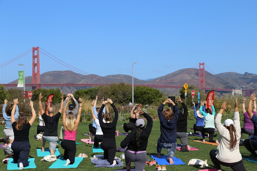 Group of people doing yoga at Outpost Meadow with the Golden Gate Bridge in the background.